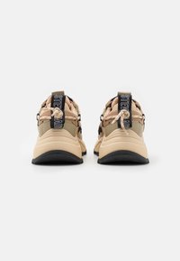 Baskets de sport beiges avec des matériaux en maille et synthétiques, des pattes de talon noires contrastantes et des semelles texturées. Lacs élastiques pour un ajustement facile.