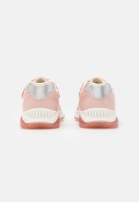 Rosa småbarns sneakers med vita sulor, silverfärgade hälaccenter och rosa gummiyttersulor, visade bakifrån på en vit bakgrund.