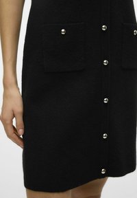 Vestido negro de fieltro con dos bolsillos frontales, detalles de botones plateados en el centro y una silueta ajustada con mangas cortas.