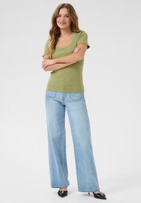 Top de manga corta acanalado en verde oliva con borde de encaje, combinado con vaqueros de pierna ancha azul claro y zapatos negros de punta.