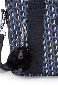 Wielopatternowa torba w odcieniach niebieskiego i czarnego z teksturowaną powierzchnią, z pluszowym czarnym breloczkiem w kształcie goryla przymocowanym do srebrnego łańcuszka.