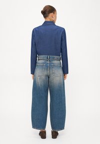 Temna modra denim srajca s ovratnikom, v kombinaciji s svetlo modrimi širokimi hlačami, ki imajo zbledel videz in dva zadnja žepa. Rjavi čevlji.