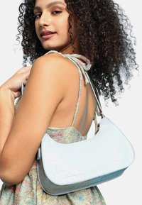 Ljusblå handväska med krokodilprägling, böjd silhuett, slät yta och axelrem, stylad med en flerfärgad klänning.