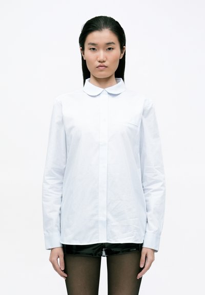 Chemise bleu clair boutonnée en tissu texturé, avec un col doux, des manches longues et une petite poche poitrine.