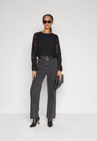 Black lace top with long sleeves, high-waisted dark gray jeans, black belt with gold buckle, black handbag, and pointed black heels.