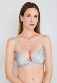 Brasiletta grigia a righe con ferretto, dotata di spalline regolabili e dettagli in metallo dorato, caratterizzata da un design liscio e supportivo e una scollatura profonda.