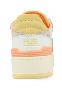 Witte en lichtgrijze sneaker met een oranje accent, voorzien van een textuurzool, zachte suède bekleding en het "HUB" logo op de hiel.