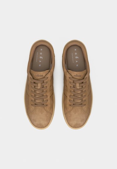 Ζευγάρι από μπεζ αθλητικά παπούτσια χαμηλής κορυφής από σουέντ με κορδόνια στο ίδιο χρώμα, επωνυμίες στις εσωτερικές σόλες και λαστιχένιες σόλες, παρουσιαζόμενα από πάνω σε λευκό φόντο.
