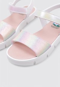 Sandalias de punta abierta con una suela de goma blanca, que cuentan con una correa iridiscente brillante y una plantilla suave de color rosa. Incluye una correa ajustable en el tobillo.