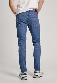 Modre denim hlače s ožjim krojem, zadnjimi žepi in rjavim usnjenim značko na pasu; v kombinaciji s sivo-belimi supergami.