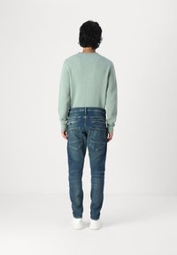 Mint green knitted sweater with a round neckline, paired with blue denim jeans featuring a faded appearance and multiple back pockets.