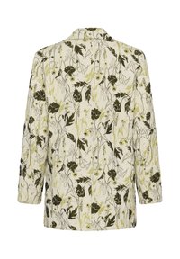 Blazer crème avec des motifs floraux et de feuilles vert foncé et jaune clair visibles sur le dos et les manches.