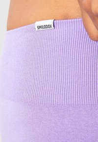 Fioletowy, prążkowany pas wykonany z materiału, z białą metką z napisem "SMILODOX". Tekstura jest miękka i elastyczna, zaprojektowana z myślą o komforcie.
