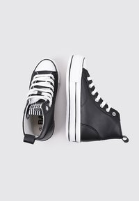Baskets montantes noires avec des lacets blancs et des accents rayés. Présentent une semelle en caoutchouc noire avec des bordures blanches et une languette au talon.