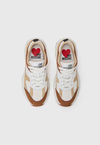 Sneakers med en hvit mesh-overdel, tan og brun semsket lær, tykke gummiflex, og "LOVE MOSCHINO" trykte innleggssåler og etiketter.