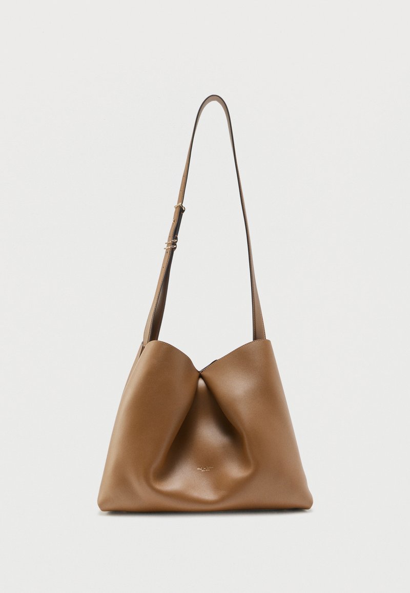 Καφέ δερμάτινη τσάντα ώμου με ρυθμιζόμενο λουρί, μαλακό, χαλαρό σχέδιο και διακριτικό ανάγλυφο λογότυπο στο μπροστινό μέρος πάνω σε μονόχρωμο φόντο.