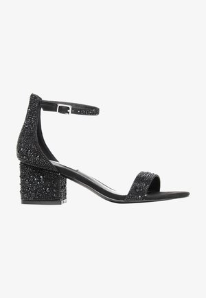 Sandales à talons noires avec une bride de cheville, ornées de perles noires et de strass, et dotées d'un talon bloc texturé.