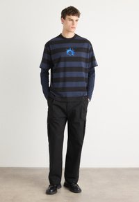 Black and blue striped T-shirt with a sun graphic, layered over a long-sleeve shirt. Paired with black cargo pants and black shoes.