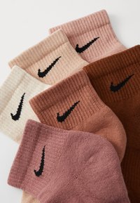 Sechs Paar Baumwollsocken in verschiedenen Beigetönen, Rosa und Braun, jeweils mit einem schwarzen Nike-Logo und gerippten Bündchen.