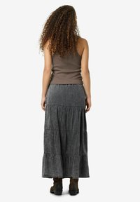 Tamsiai pilkos medžiagos maxi sijonas su susiraukšlėjusiais sluoksniais ir subtilia tekstūra, derinamas su prigludusia rudą marškinėliais be rankovių ir rudomis čiurnos botais.