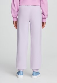 Pantaloni della tuta in pile lilla con vita e polsini elasticizzati, caratterizzati da una texture morbida. Abbinati a sneaker in tela azzurra chiara.