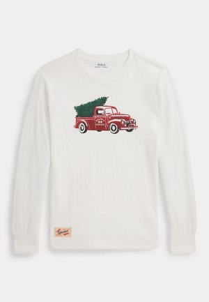Hvid langærmet skjorte med et rødt vintage lastbilmotiv, der bærer et juletræ, og en lille beige mærkeflap nær kanten.