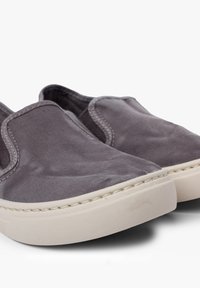 Grijze canvas instappers met contrasterende beige rubberen zolen, met ronde randen en zichtbare stiksels langs de naden.