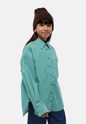 Chemise à rayures vertes et blanches avec une coupe décontractée, dotée d'une poche poitrine et de manches longues. Associée à un bonnet en tricot marron.