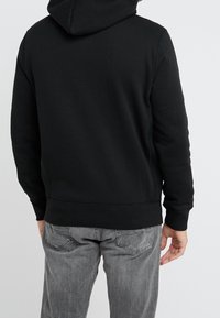 Sudadera con capucha negra de textura de forro polar, con el dobladillo y los puños acanalados. La parte trasera es sencilla, sin logotipos ni patrones visibles.