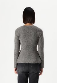 Grå ribbestrikket genser med lange ermer, tettsittende liv og peplum-design. Kjøttete strikket stoff. Bært med høyt liv, mørke jeans.