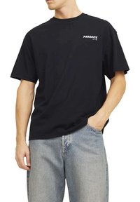 T-shirt in cotone nero con maniche corte, vestibilità rilassata; presenta la scritta "PARADISE EST '90" stampata in bianco nella zona sinistra del petto.