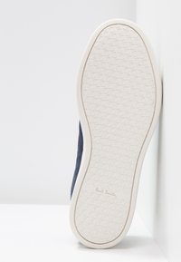 Navy suede sneaker with a white rubber sole featuring a textured pattern. The sole displays a logo and is slightly raised at the heel.