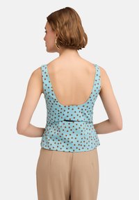 Top peplum azzurro con pois marroni, caratterizzato da una profonda scollatura a forma di U sul retro e spalline larghe, realizzato in tessuto morbido.