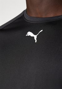 Sort atletisk skjorte lavet af glat stof, med rund halsudskæring og et hvidt Puma-logo trykt på brystet.