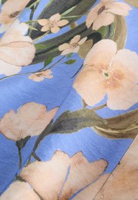 Tissu bleu doux avec de grandes fleurs pêche pâle et des feuilles vertes dans un motif floral détaillé et naturaliste.