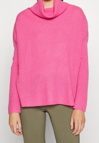 Maglione rosa lavorato a maglia con collo ad anello, tessitura a coste e maniche lunghe. Presenta una vestibilità comoda e spacchi laterali sull'orlo.