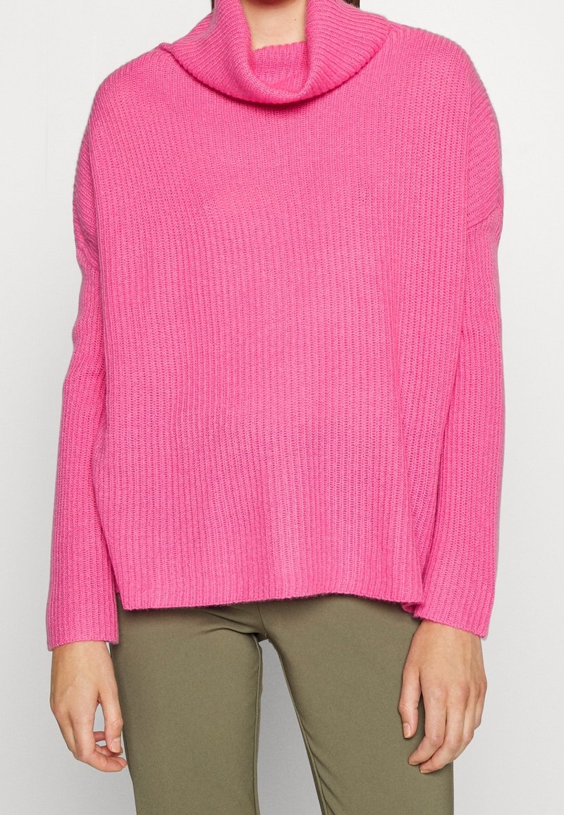 Maglione rosa lavorato a maglia con collo ad anello, tessitura a coste e maniche lunghe. Presenta una vestibilità comoda e spacchi laterali sull'orlo.