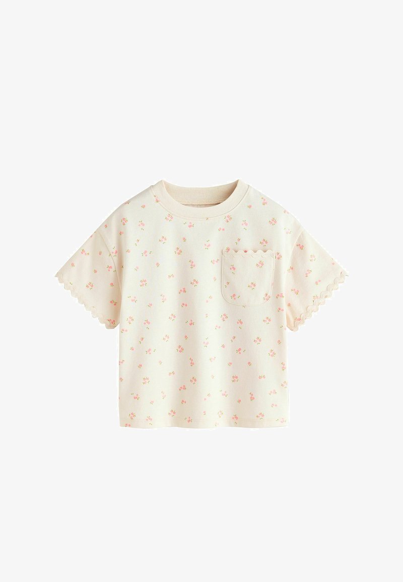 Camiseta de manga corta color crema con pequeño estampado floral rosa, bordes ondulados en las mangas y un bolsillo delantero con borde ondulado.