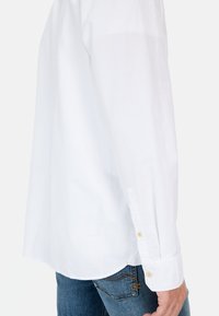 Witte blouse met lange mouwen en een doorlopende manchet, gemaakt van katoen, met een strak ontwerp en een gladde textuur, gecombineerd met blauwe denim jeans.