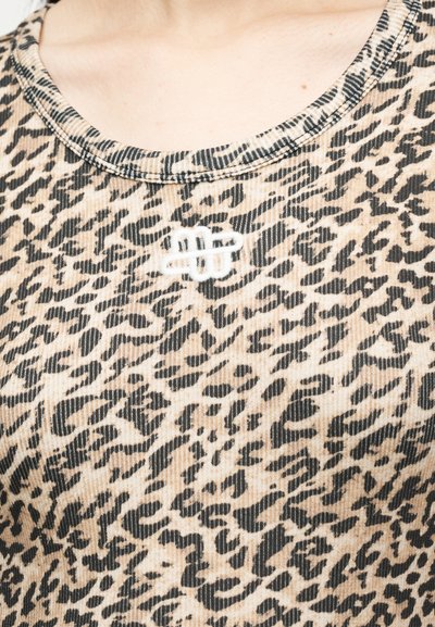 Κοντινό πλάνο ενός ατόμου που φοράει ριπ τοπ με λεοπάρ σχέδιο και μικρό λευκό κεντημένο λογότυπο κοντά στη λαιμόκοψη.