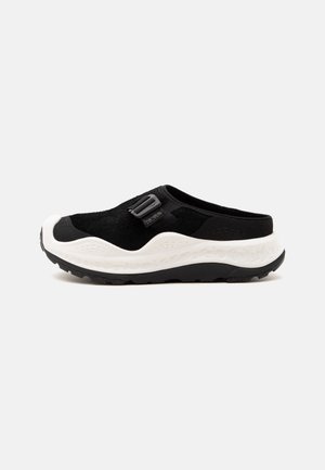 Čierna slip-on teniska s bielou hrubou podrážkou, nastaviteľným remienkom a textúrovaným dezénom, navrhnutá pre bežné alebo vonkajšie nosenie.