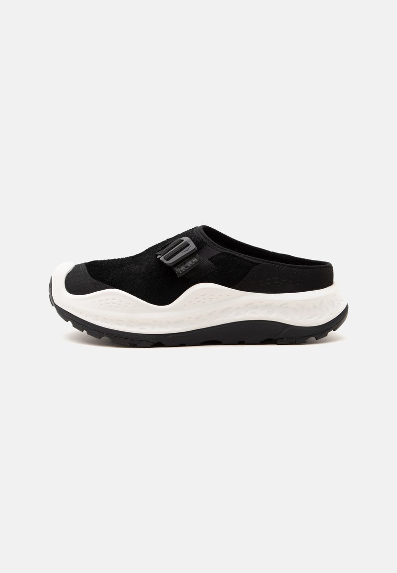 Μαύρο sneaker χωρίς κορδόνια με λευκή παχιά σόλα, ρυθμιζόμενο λουράκι και υφή στο πέλμα, σχεδιασμένο για καθημερινή ή υπαίθρια χρήση.