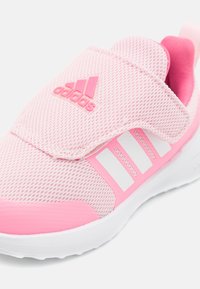 Scarpa sportiva rosa con parte superiore in rete, dotata di una fascia in Velcro e tre strisce bianche sui lati. Accenti rosa solidi sulla suola.