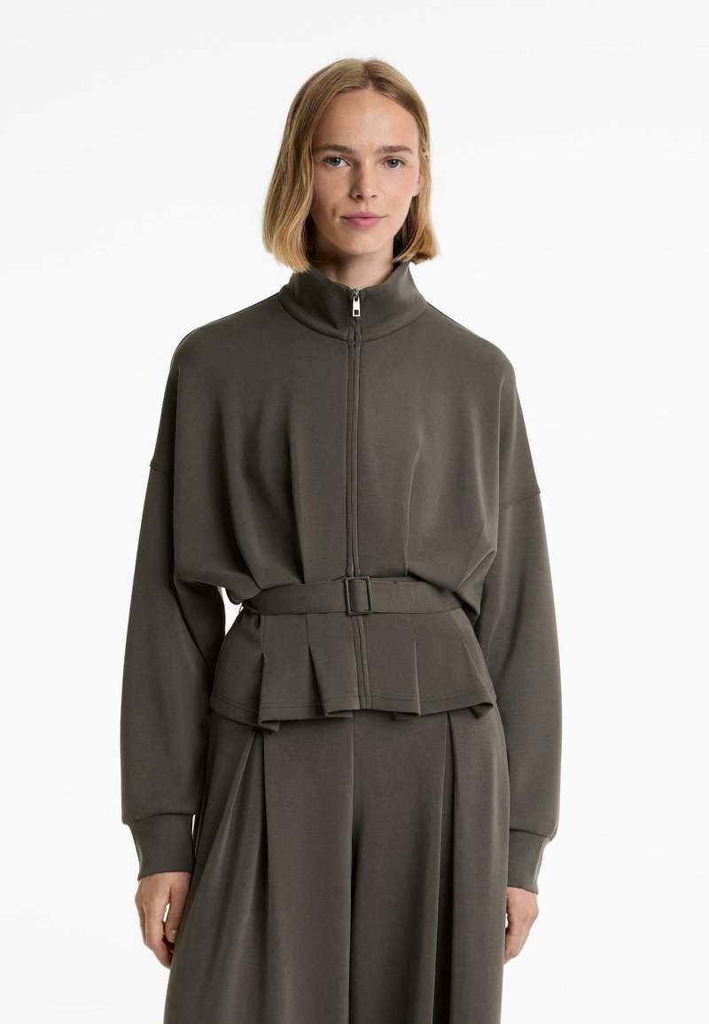 Temno olivno zelen zip-jaket z visoko ovratnikom, ohlapen kroj, pasom in plisiranjem na robu. Gladka tekstura tkanine.