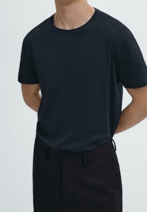 Dark navy short-sleeve t-shirt in a smooth cotton blend, featuring a round neckline and a regular fit, paired with dark striped trousers.