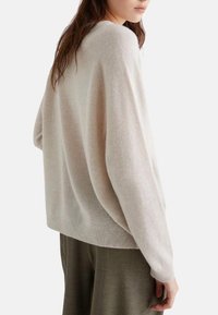 Maglione oversize beige chiaro con una texture morbida, maniche larghe e scollatura rotonda, abbinato a pantaloni verde oliva.