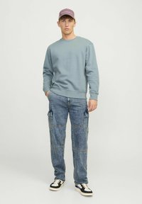 Felpa azzurro chiaro con collo a giro, abbinata a pantaloni cargo blu sbiaditi con tasche a patta. Sneakers bianco e nero aggiungono un contrasto.