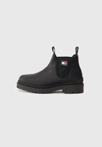 Botín Chelsea negro con panel lateral elástico, lengüetas de tirón, suela gruesa y parche con el logo de Tommy Jeans en el lateral.