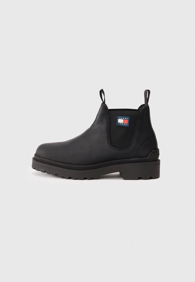 Botín Chelsea negro con panel lateral elástico, lengüetas de tirón, suela gruesa y parche con el logo de Tommy Jeans en el lateral.