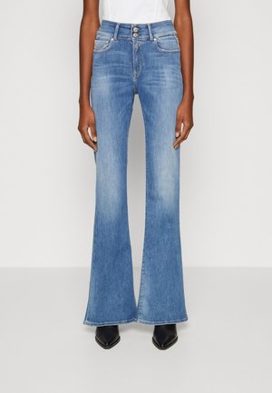 Hoikka vyötärö, vaaleansiniset korkeavyötäröiset liehuvat farkut, joissa on nappisuljin, yhdistetty valkoiseen yläosaan ja mustiin kärjestään teräviin saappaisiin.